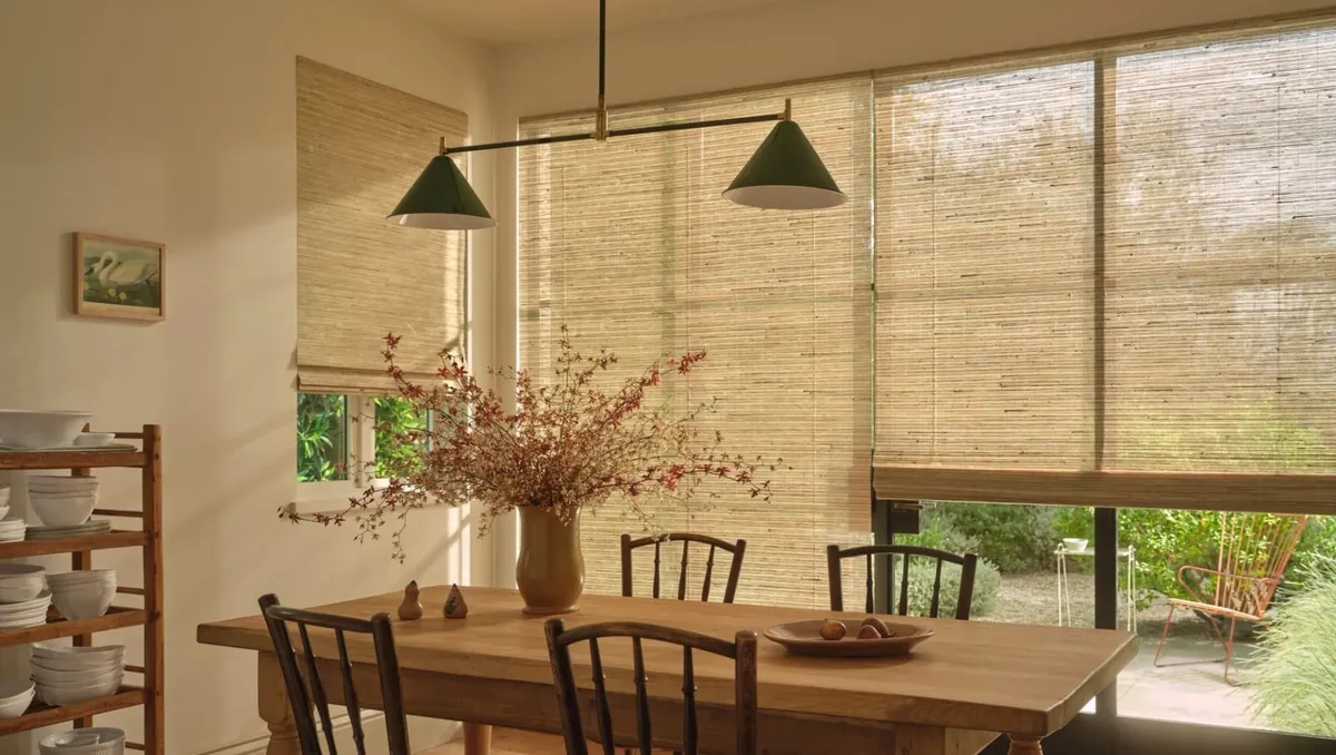 Natural woven wood shades on a corner window and a large patio window in a sunlit dining room with a farmhouse table