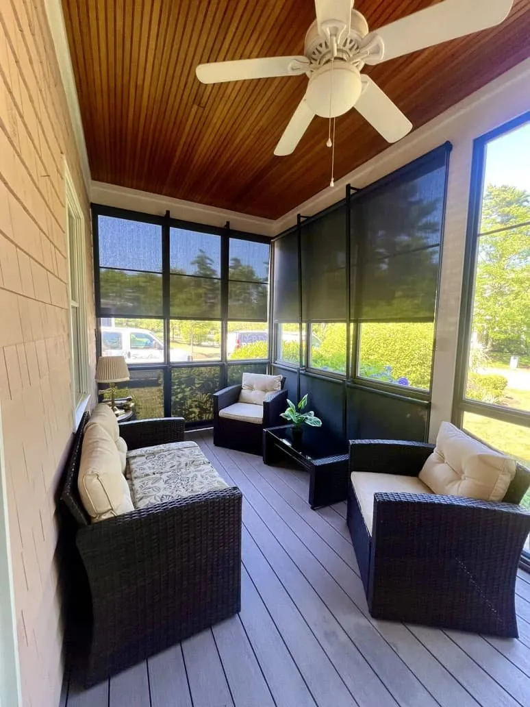 Dark solar screen shades lowered around a screened porch with wicker seating and a wood ceiling