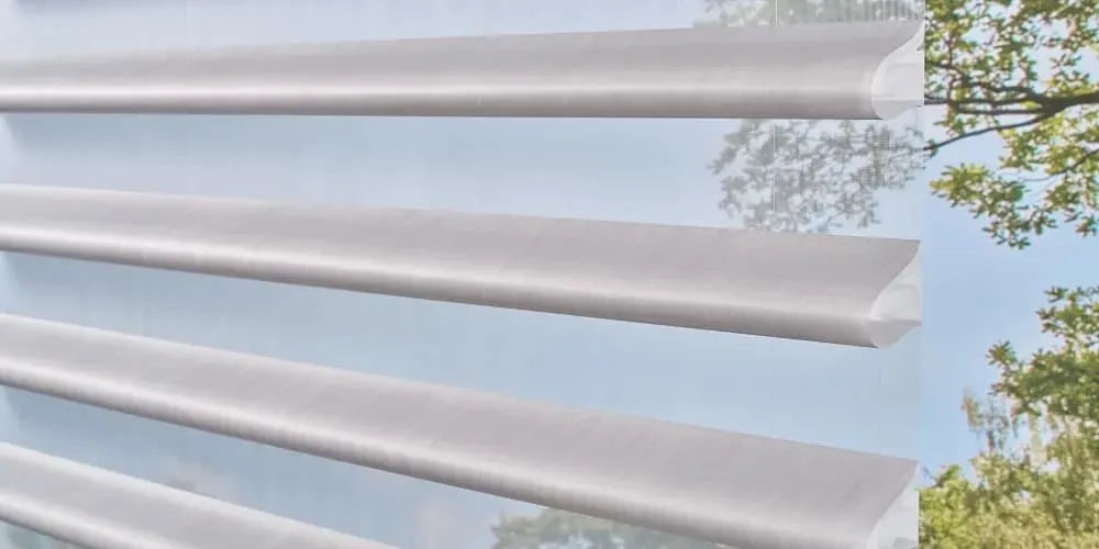 Close-up of soft grey fabric vanes on a sheer backing, with trees and sky visible behind