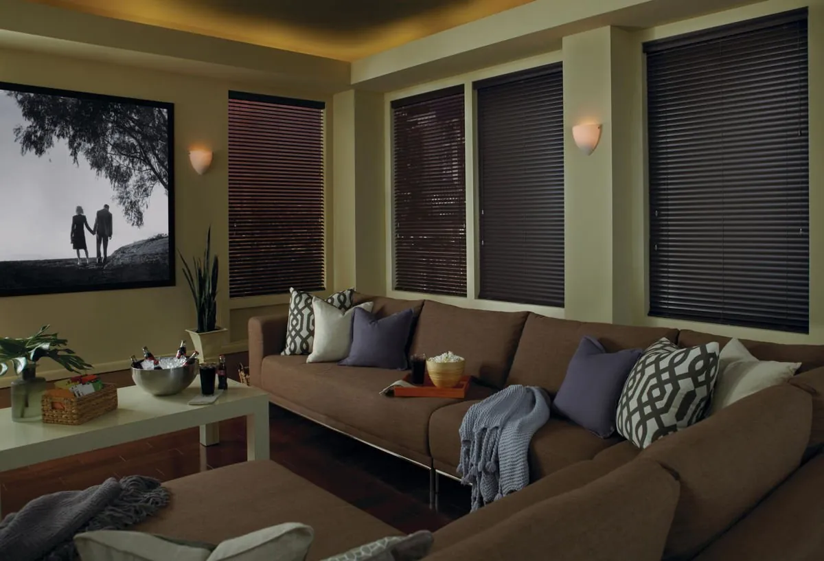 Dark espresso horizontal blinds closed on four windows in a dim media room with a brown sectional and a large screen
