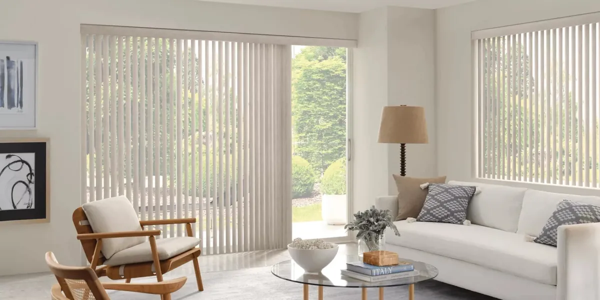 Cream vertical blinds on a sliding patio door and side window in a bright living room with a white sofa and glass coffee table