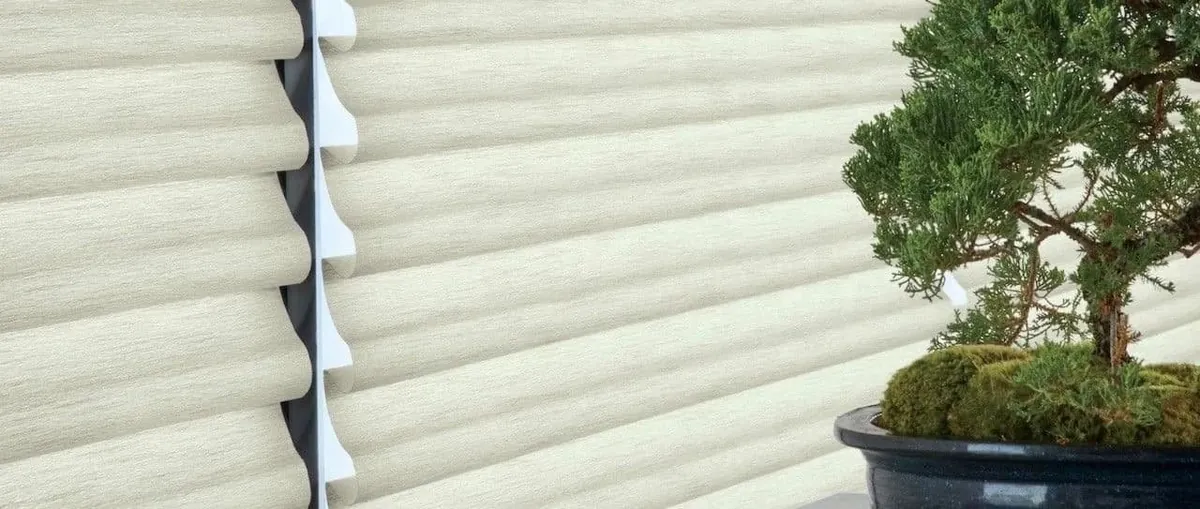 Close-up of a cream sheer shade with soft horizontal fabric vanes, side profile visible, beside a bonsai tree