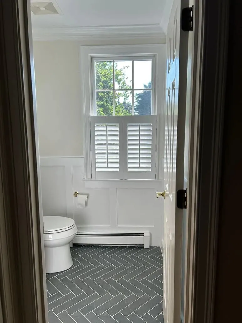 White cafe-style plantation shutters on the lower half of a powder room window, seen through the open door