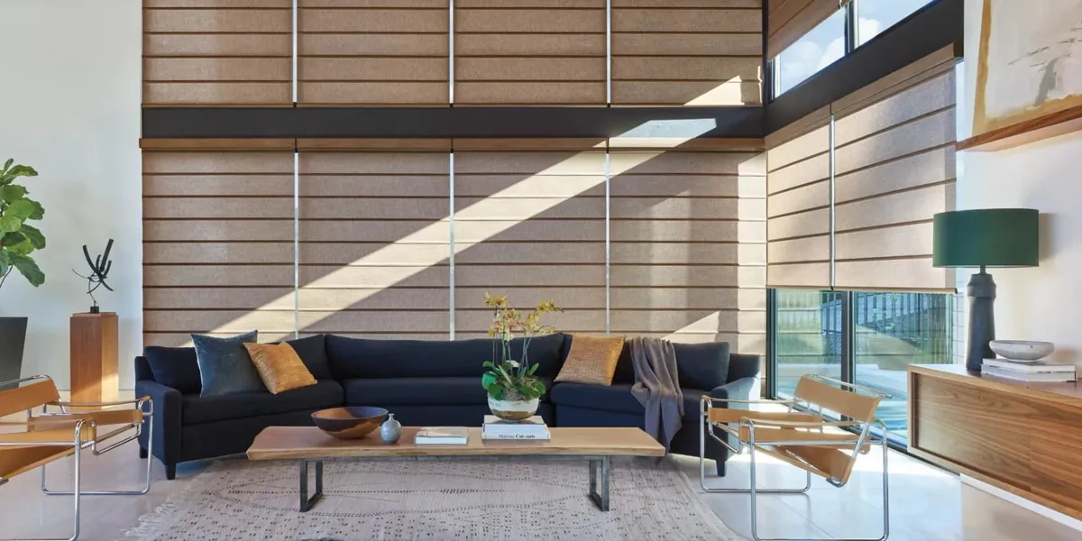 Tan fabric shades with horizontal bands covering a double-height window wall behind a navy sectional in a modern living room