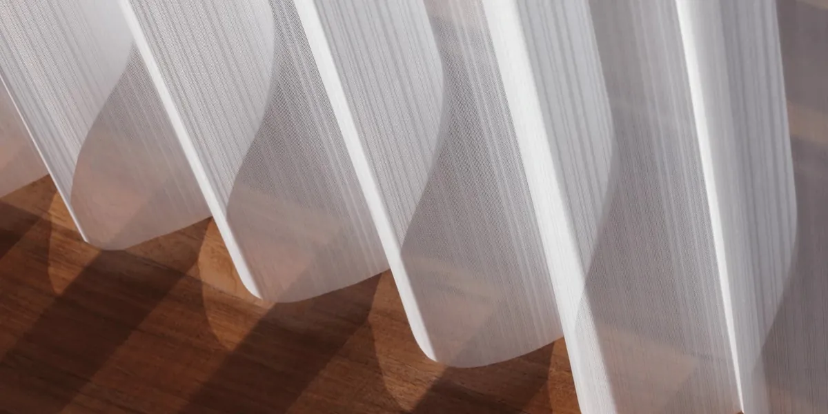 Close-up of a white sheer vertical shade with soft fabric vanes casting shadows on a warm wood floor