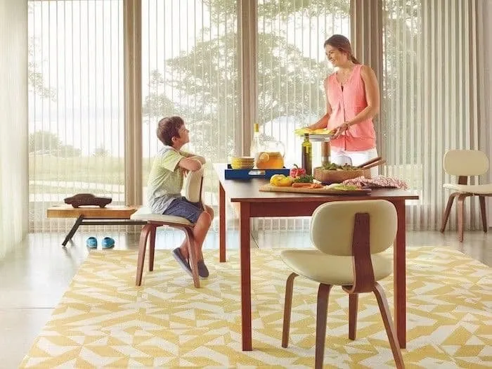 Floor-to-ceiling vertical sheer panels on a wall of windows in a dining room, with a woman serving and a boy seated at the table